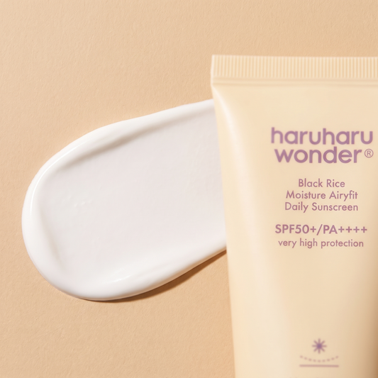 Samtige Textur der Haruharu Wonder Black Rice Airy-fit Sonnencreme auf hellem Stein, Tube angeschnitten daneben