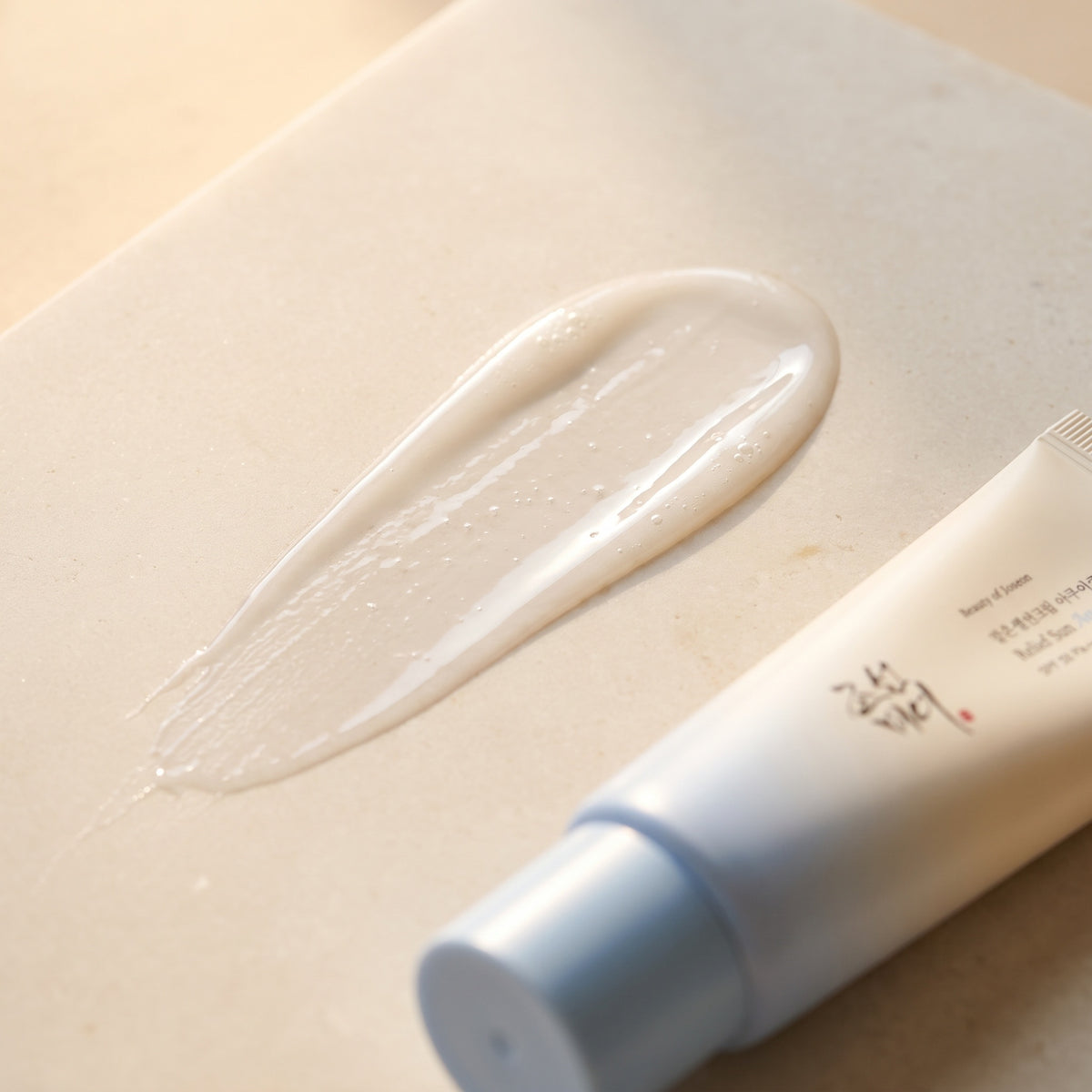 Cremetextur der Beauty of Joseon Relief Sun Aqua-Fresh auf hellem Stein, die Tube liegt angeschnitten daneben