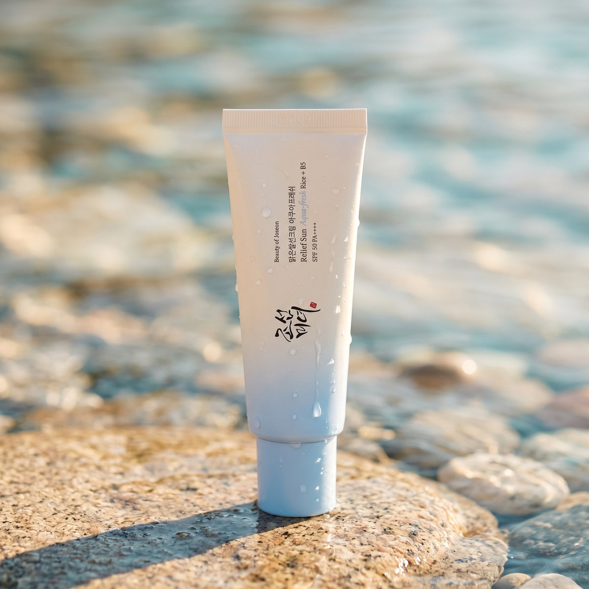 Beauty of Joseon Relief Sun Aqua-Fresh steht auf einem nassen Stein am Wasser, Tropfen laufen an der Tube herunter