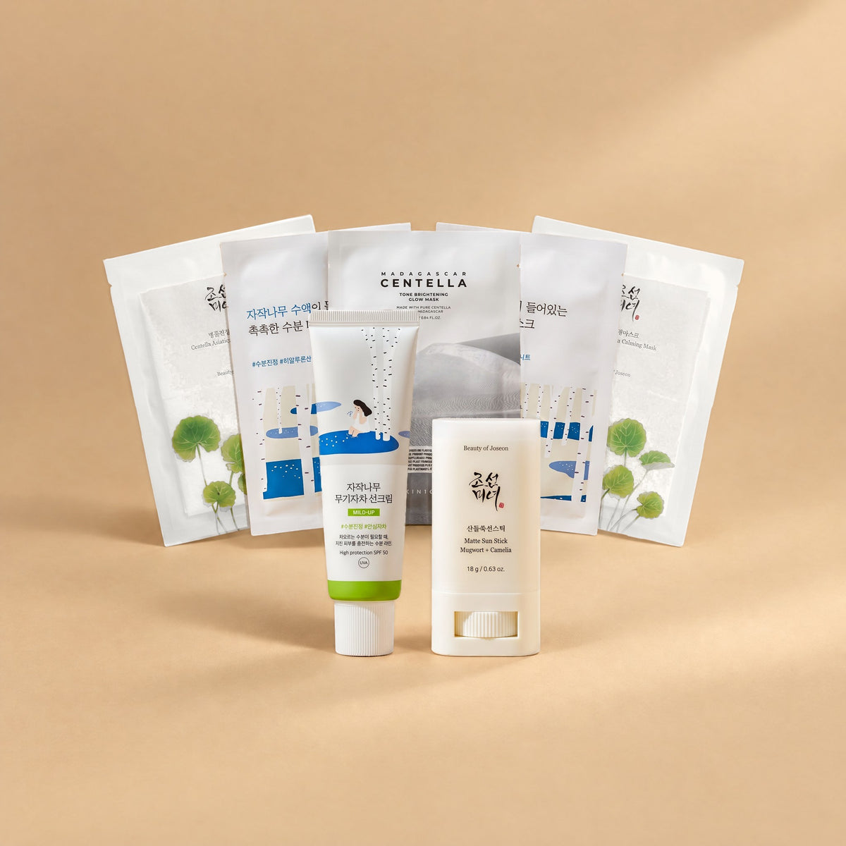 Beruhigungs-Set von Go & Glow: Round Lab Birch Juice Mild-Up Sonnencreme SPF 50, Beauty of Joseon Matte Sun Stick und fünf Tuchmasken als Fächer auf sandfarbenem Hintergrund