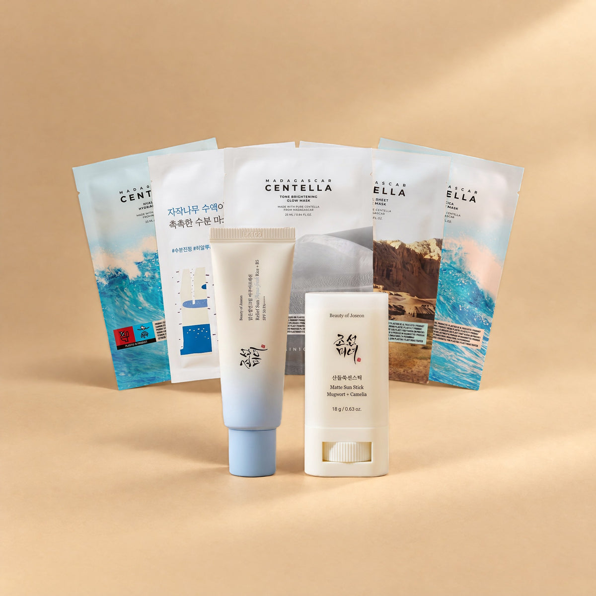 Feuchtigkeits-Set von Go & Glow: Beauty of Joseon Relief Sun Aqua-Fresh Sonnencreme SPF 50, Beauty of Joseon Matte Sun Stick und fünf Tuchmasken als Fächer auf sandfarbenem Hintergrund