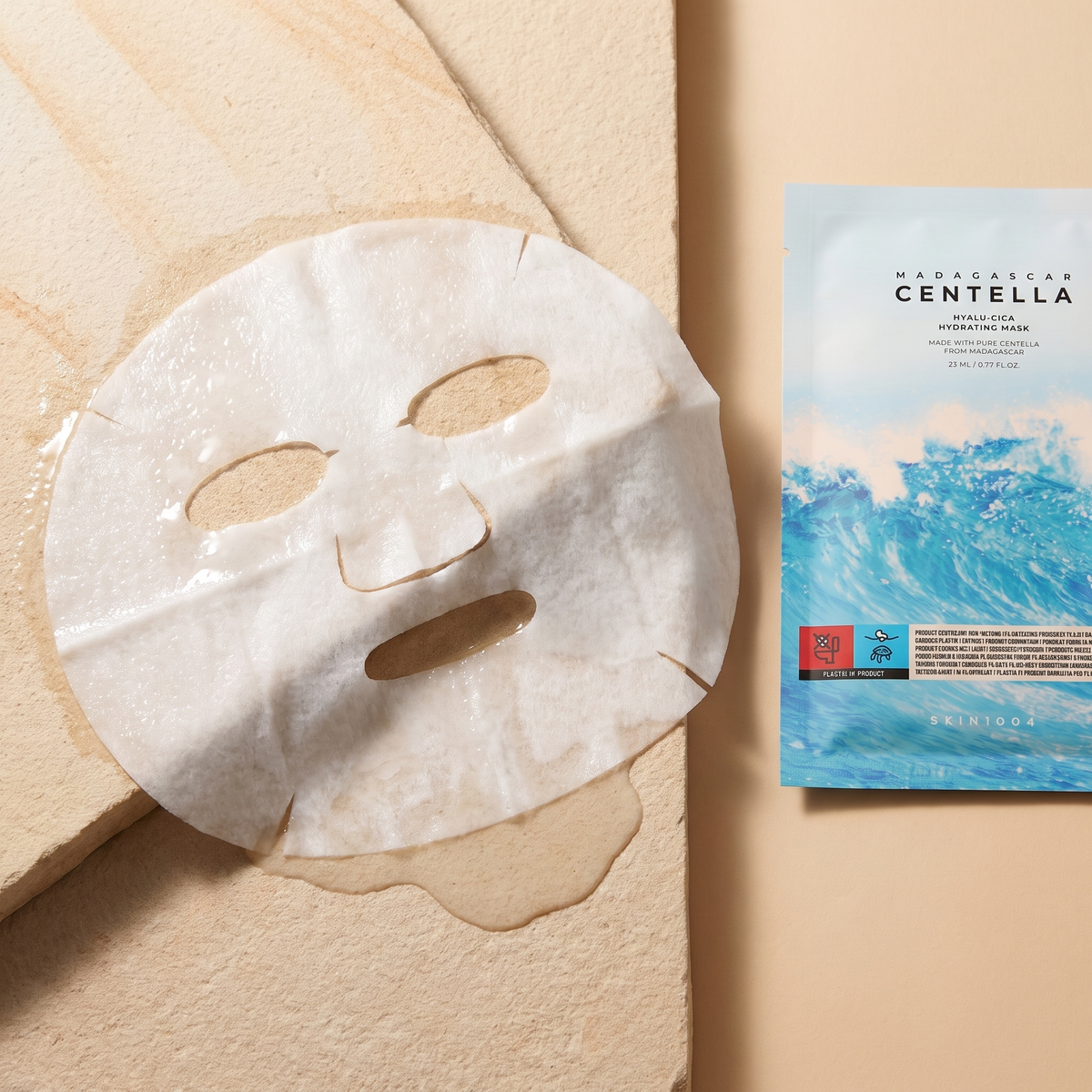 Nasses Tuch der SKIN1004 Hyalu-Cica Hydrating Mask auf hellem Stein, Sachet angeschnitten daneben