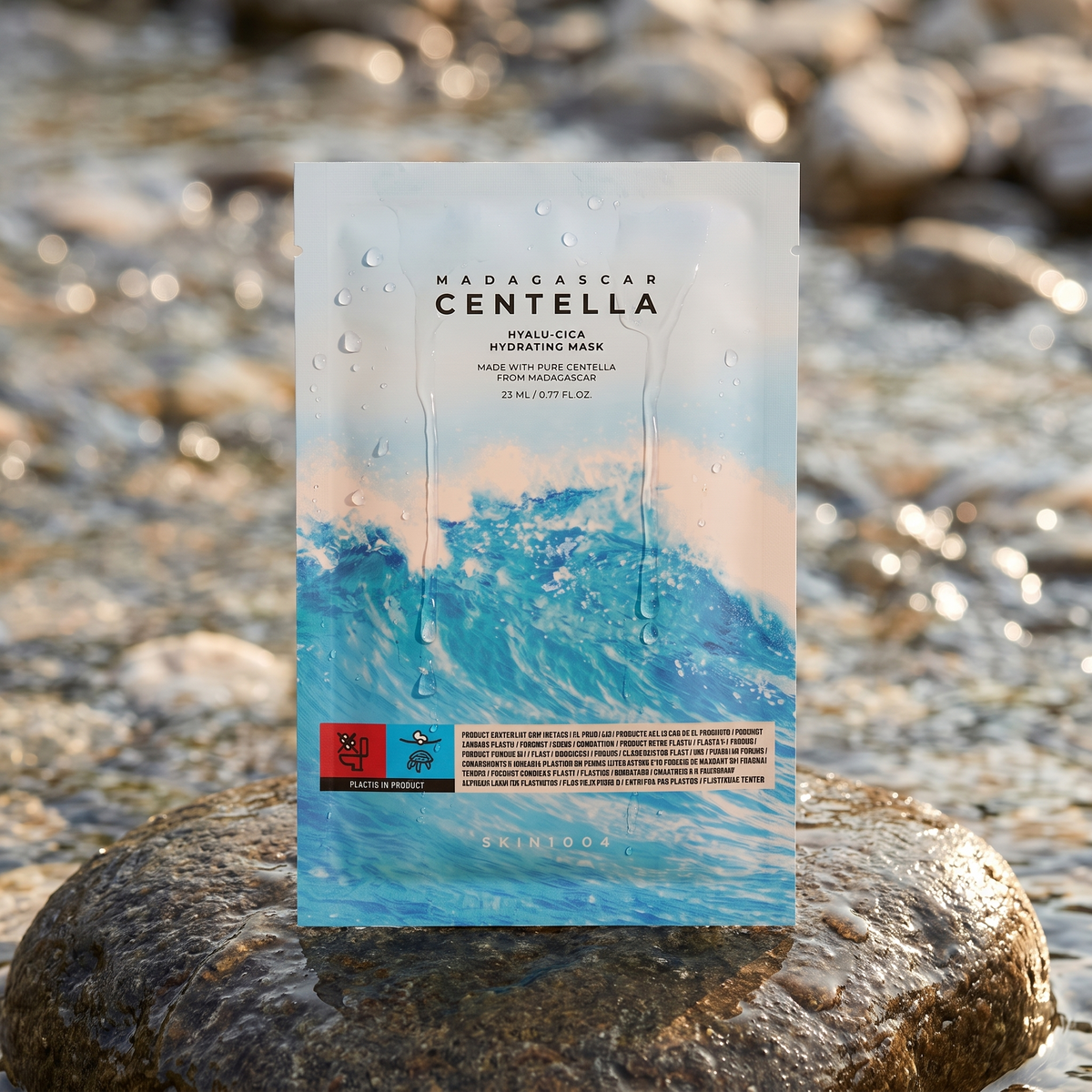 SKIN1004 Hyalu-Cica Hydrating Mask lehnt an einem nassen Stein am Bach, Wassertropfen auf der Folie