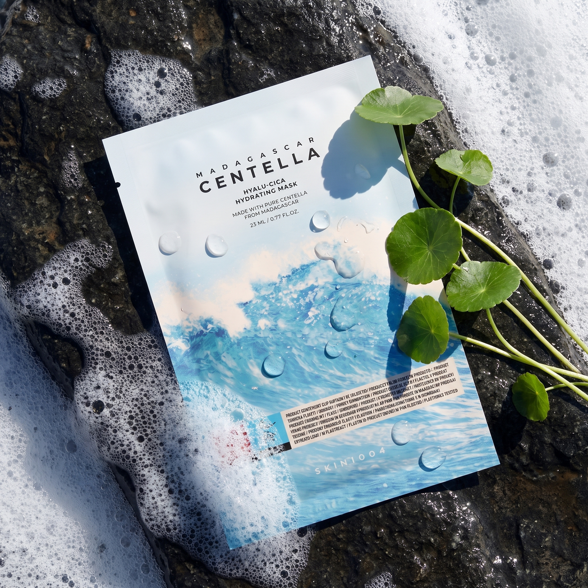 SKIN1004 Hyalu-Cica Hydrating Mask liegt auf nassem Küstenfels mit Meerschaum, daneben Centella-Blätter