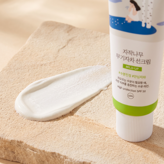Cremetextur der Round Lab Birch Juice Mild Up Sonnencreme auf hellem Stein, Tube angeschnitten daneben