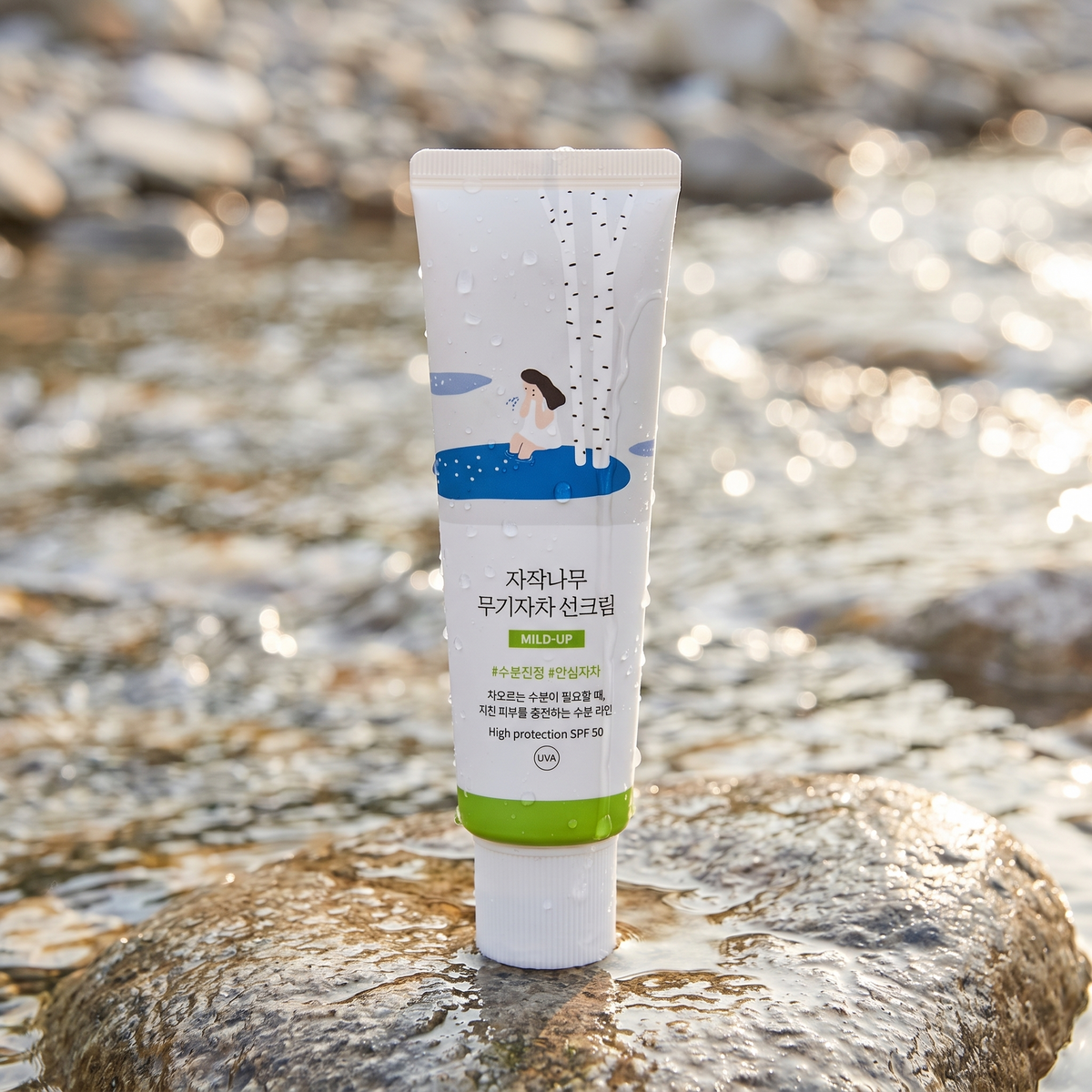 Round Lab Birch Juice Mild Up Sonnencreme steht auf einem nassen Stein am Bach, Wassertropfen auf der Tube