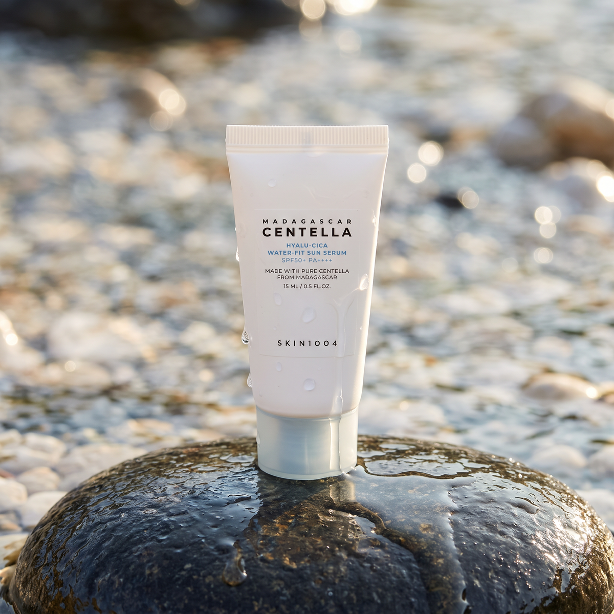 SKIN1004 Hyalu-Cica Water-Fit Sun Serum steht auf einem nassen Stein am Bach, Wassertropfen auf der Tube