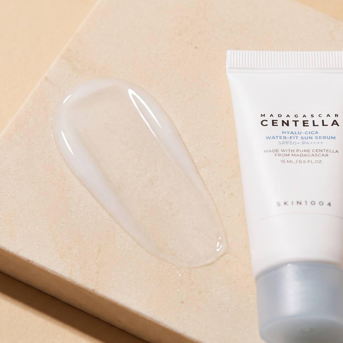Wasserklare Textur des SKIN1004 Hyalu-Cica Water-Fit Sun Serum auf hellem Stein, Tube daneben