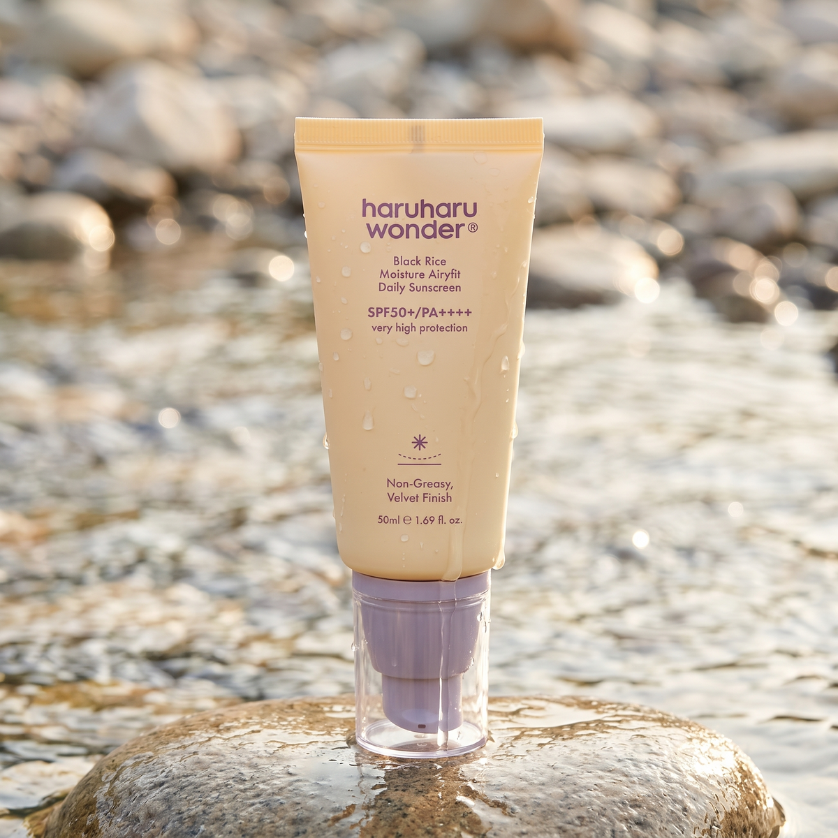 Haruharu Wonder Black Rice Airy-fit Sonnencreme steht auf einem nassen Stein am Bach, Wassertropfen auf der Tube