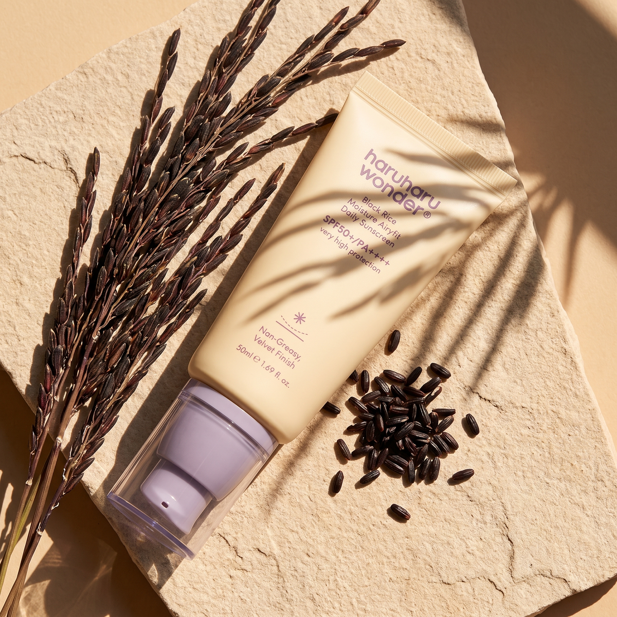 Haruharu Wonder Black Rice Airy-fit Sonnencreme liegt im Sonnenlicht auf hellem Sandstein, daneben schwarze Reisähren