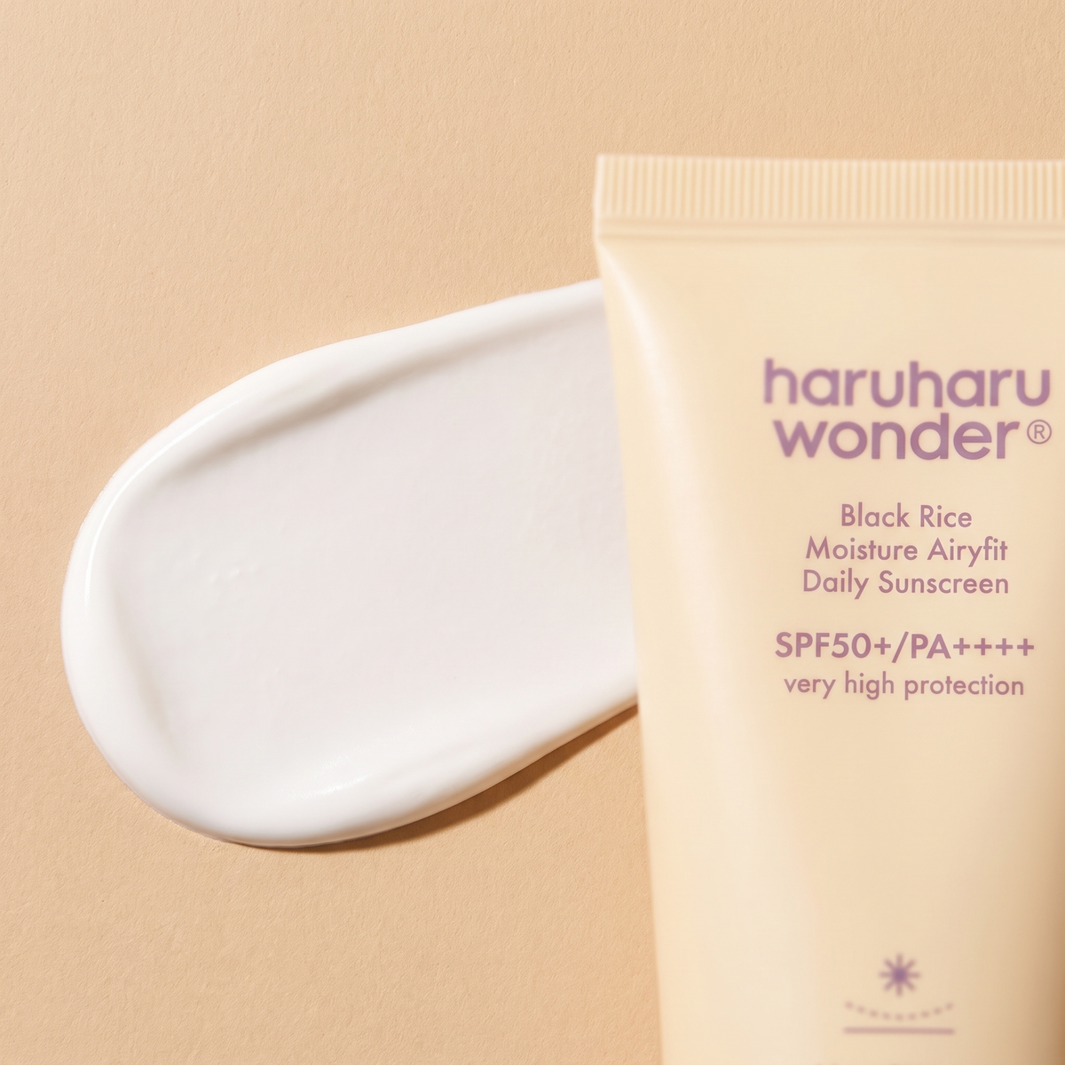 Samtige Textur der Haruharu Wonder Black Rice Airy-fit Sonnencreme auf hellem Stein, Tube angeschnitten daneben
