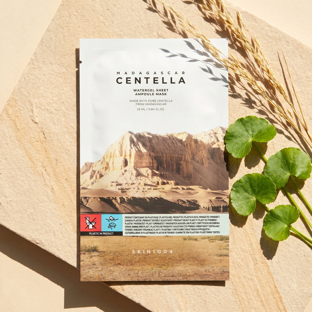 SKIN1004 Watergel Sheet Ampoule Mask liegt im Sonnenlicht auf hellem Sandstein, daneben trockene Gräser und Centella-Blätter