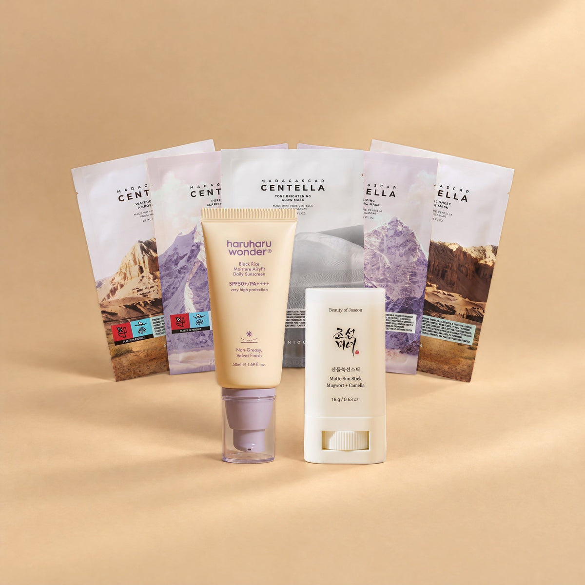 Matt-Set von Go & Glow: Haruharu Wonder Black Rice Sonnencreme SPF 50+, Beauty of Joseon Matte Sun Stick und fünf SKIN1004 Tuchmasken als Fächer auf sandfarbenem Hintergrund