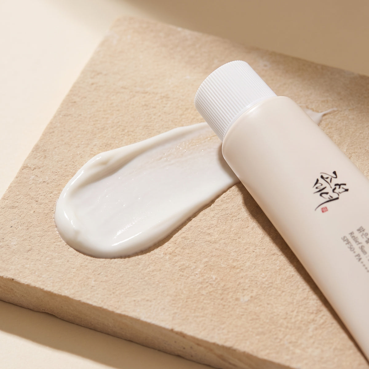 Cremetextur der Beauty of Joseon Relief Sun Rice + Probiotics auf hellem Stein, die Tube liegt angeschnitten daneben