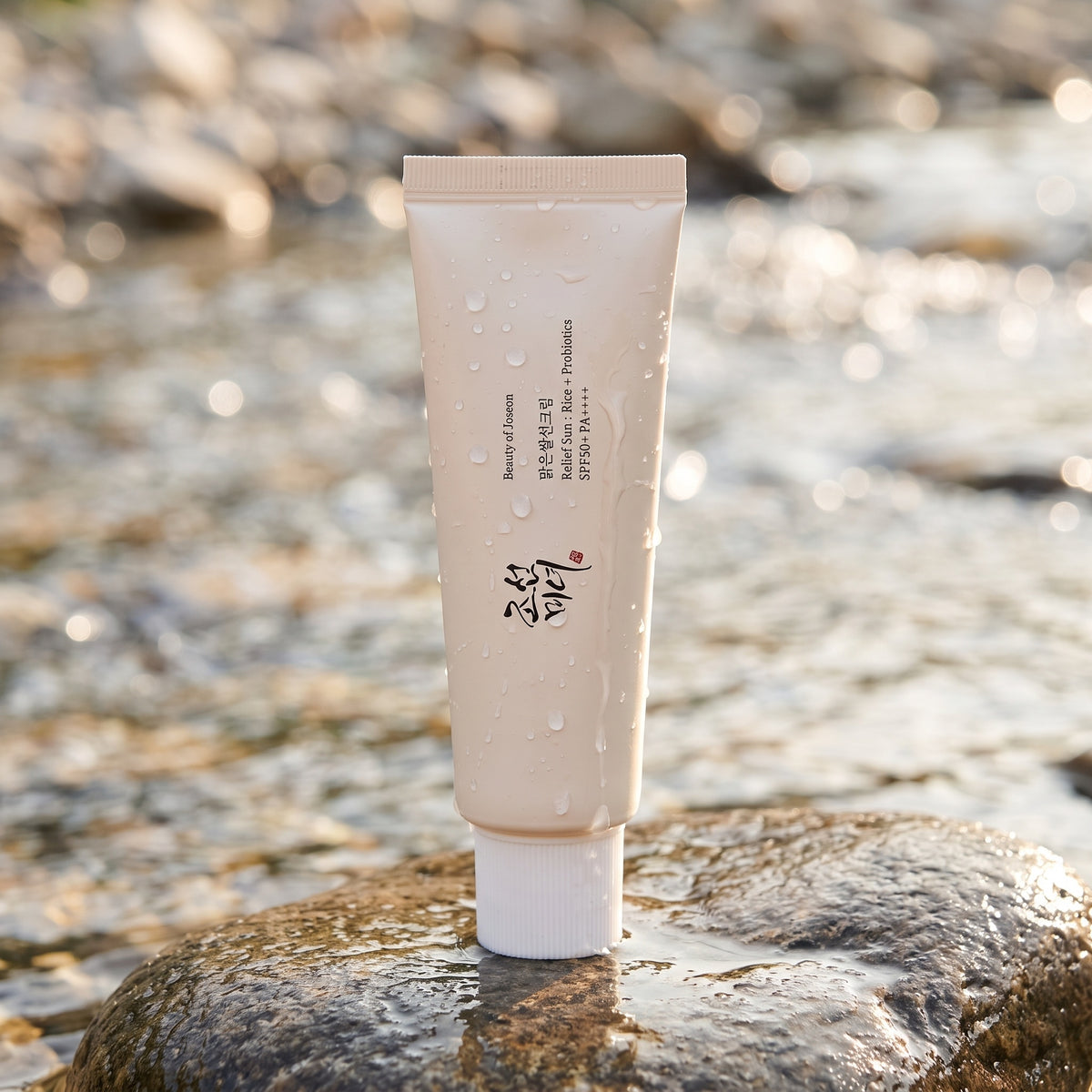 Beauty of Joseon Relief Sun Rice + Probiotics steht auf einem nassen Stein am Bach, Wassertropfen auf der Tube