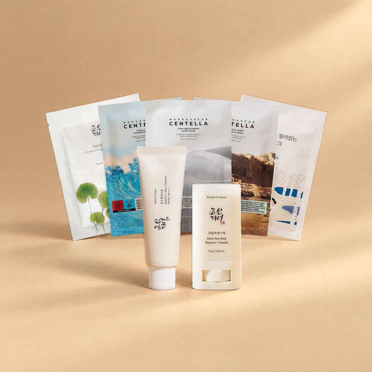 Sonnen-Routine Set von Go & Glow: Beauty of Joseon Relief Sun Rice + Probiotics Sonnencreme SPF 50+, Beauty of Joseon Matte Sun Stick und fünf Tuchmasken als Fächer auf sandfarbenem Hintergrund