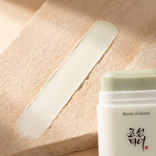 Geöffneter Beauty of Joseon Matte Sun Stick mit blassgrünem Balsam, daneben ein matter Strich auf hellem Sandstein